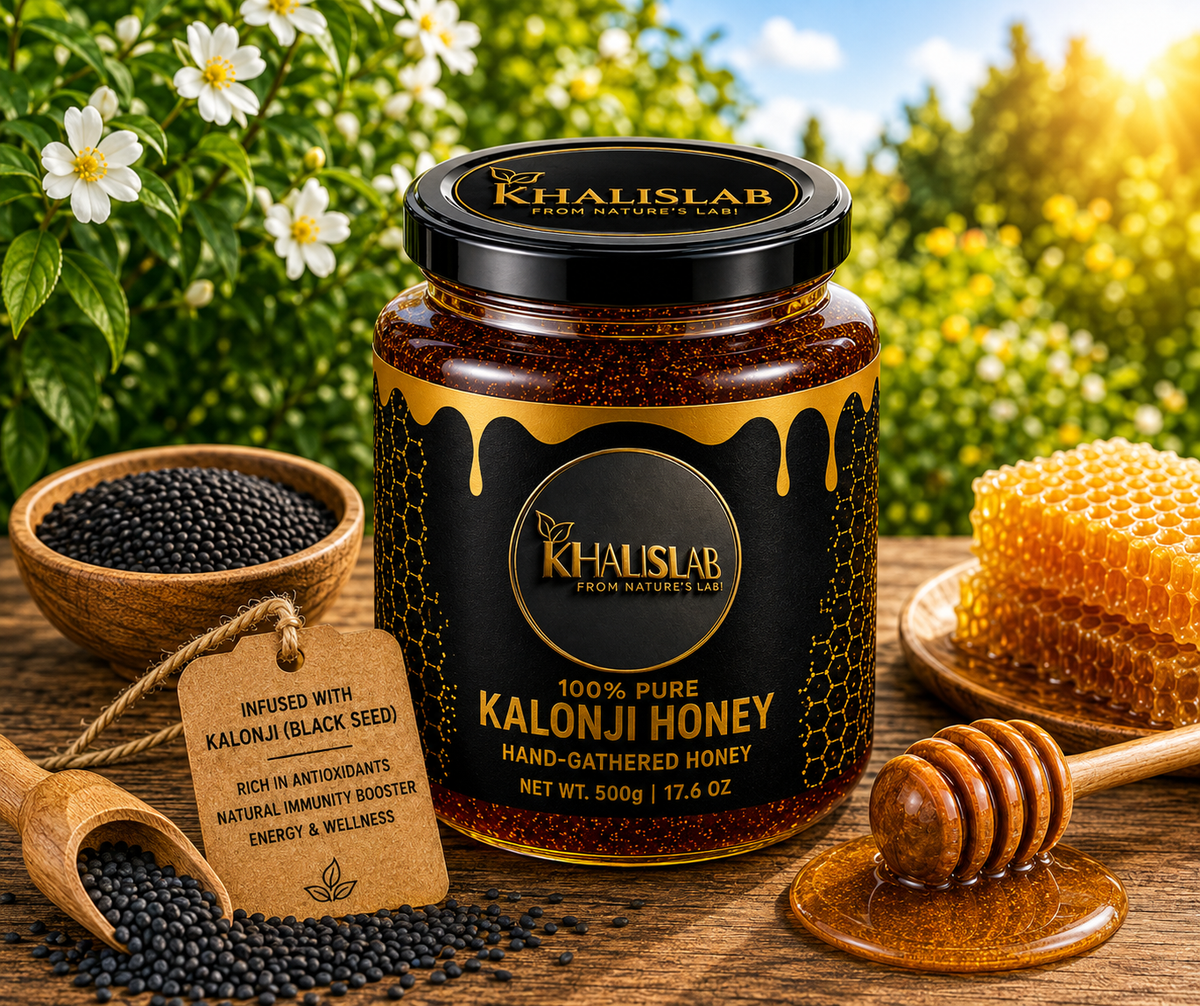 A jar of Khalislab Kalonji Honey is displayed on a rustic wooden table with a natural outdoor garden background. The jar is surrounded by props including a wooden honey dipper, a piece of raw honeycomb, a bowl of black seeds, and a wooden scoop of seeds with a descriptive paper tag.